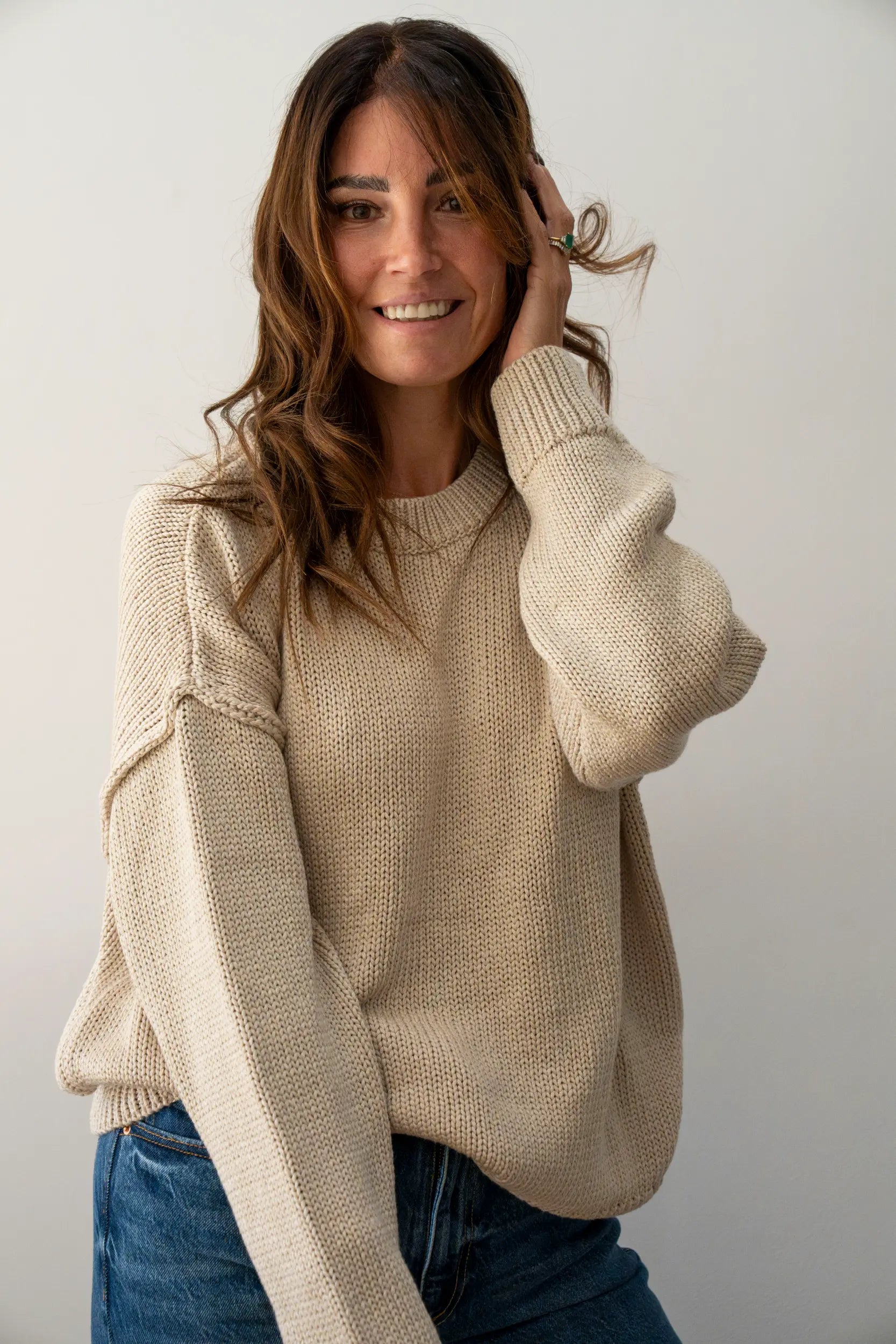 Smiling woman in a cream knit jumper wearing a wavy brunette Midi human hair wig