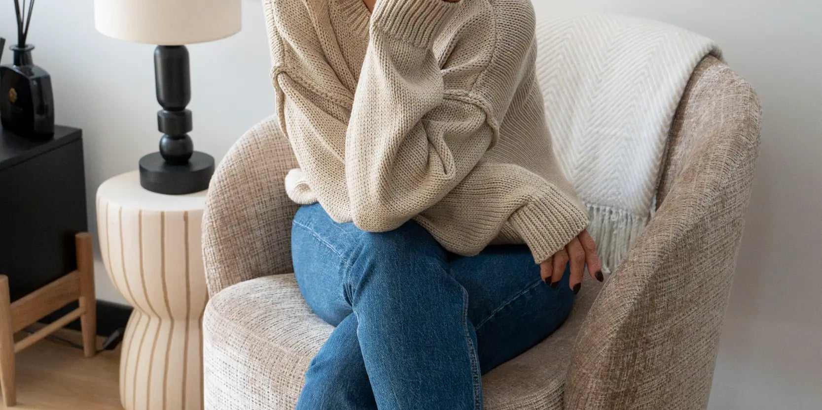 Woman with her hair in a top knot sitting in an armchair with her hand on her chin