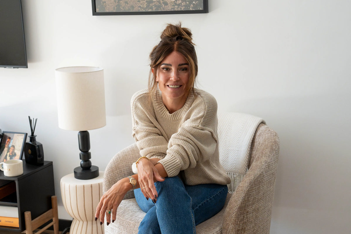 Woman with her hair in a top knot relaxing in a cream armchair in jeans and a cream jumper